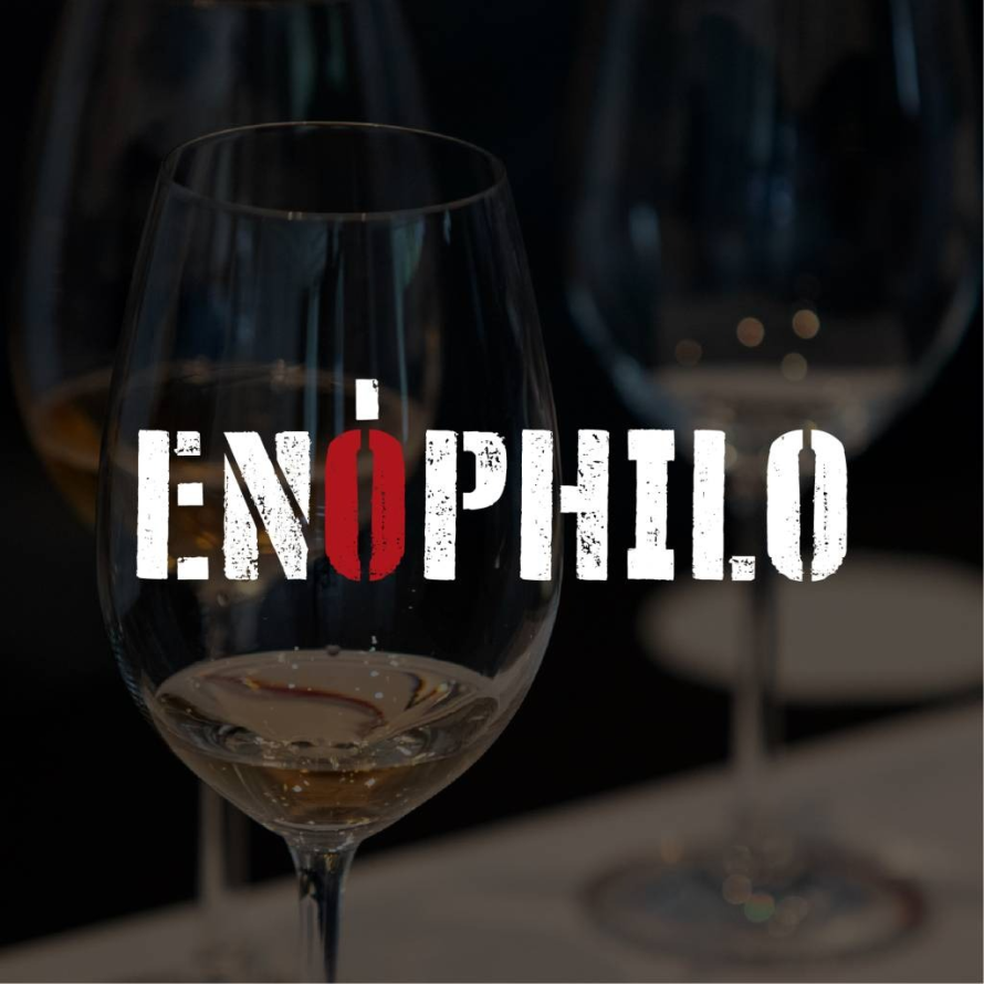 Copo de cristal com vinho branco sobre mesa de prova com o logótipo Enóphilo — plataforma de cultura e educação vínica em Portugal