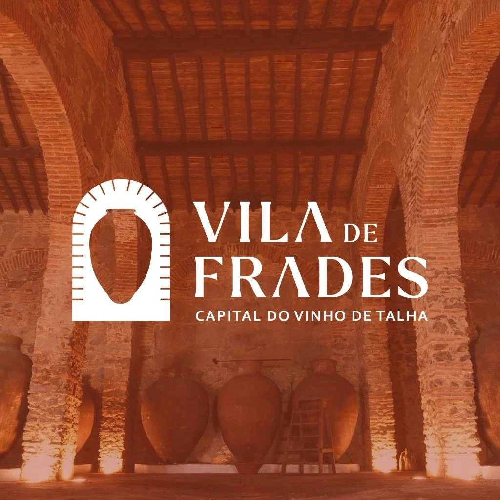 Interior de uma adega histórica com talhas de barro antigas e iluminação quente, em Vila de Frades.