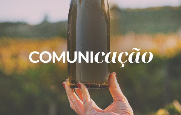 Mão feminina segura garrafa de vinho tinto contra paisagem de vinha ao pôr do sol com o texto "COMUNIcação" — comunicação e marketing vitivinícola